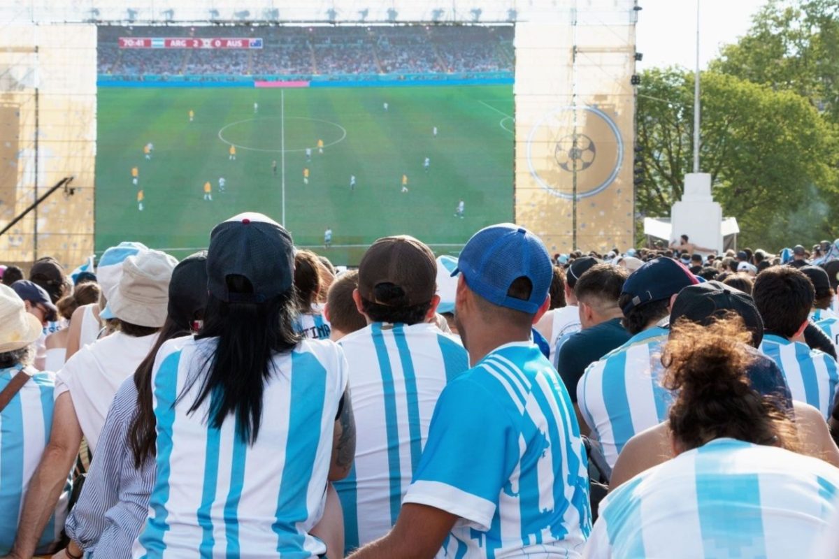 A large crowd of diverse fans watching a World Cup match on a big outdoor screen at a New York City fan zone