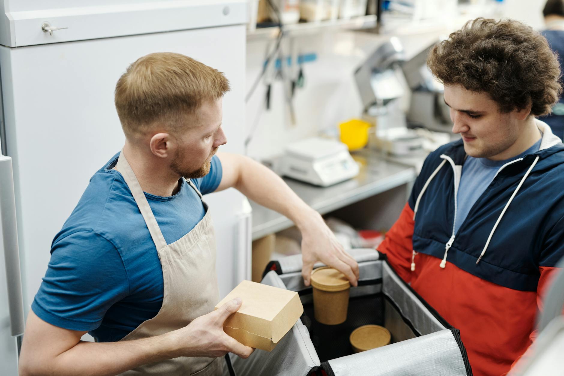 Um membro da equipe de catering carrega recipientes térmicos de alimentos durante a configuração de um serviço de buffet ao ar livre em um local de eventos.