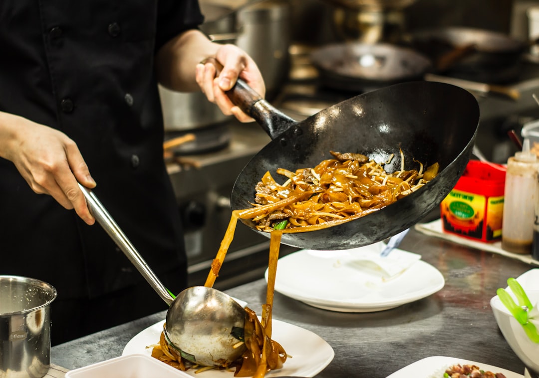 Uno chef che presenta una ciotola di noodle freddi finita e guarnita con erbe aromatiche e semi di sesamo pronta da servire