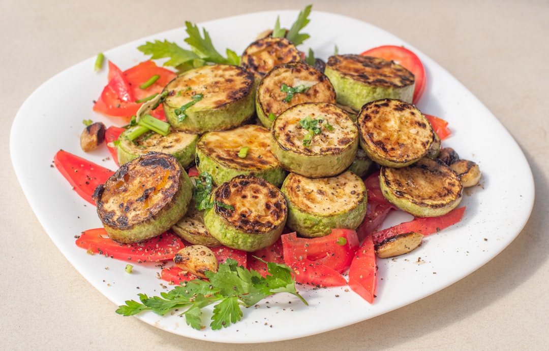 A cook arranging rested grill vegetables on a plate, their charred surfaces glistening with olive oil