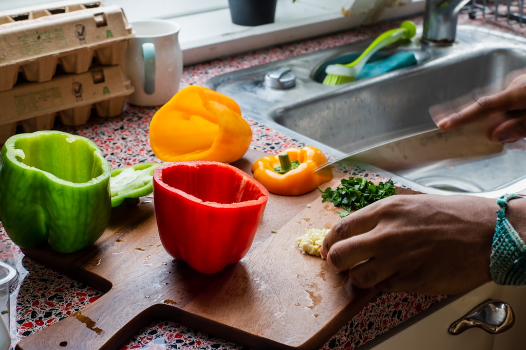 Una cuoca casalinga pela la buccia annerita dai peperoni estivi abbrustoliti su una ciotola di vetro su un piano cottura in legno in cucina.