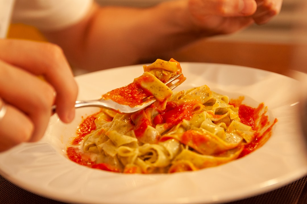 Uma pessoa coloca ragù napolitano cozido lentamente sobre uma tigela de massa curta e estriada em uma mesa de jantar de madeira