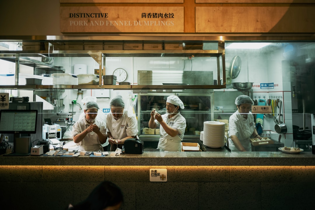 Um mentor experiente trabalha com um novo membro da equipa durante a formação de pessoal para cozinhas globais num ambiente de restaurante movimentado