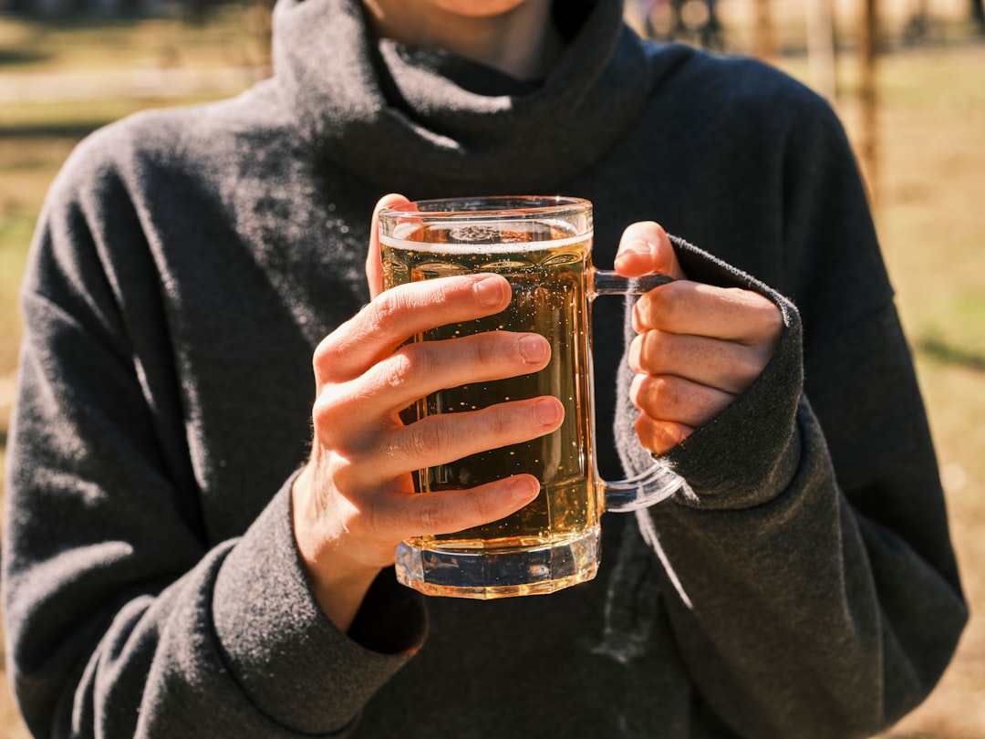 Una persona che tiene in mano un bicchiere di tè freddo all'aperto con la luce del sole che filtra attraverso le foglie sullo sfondo