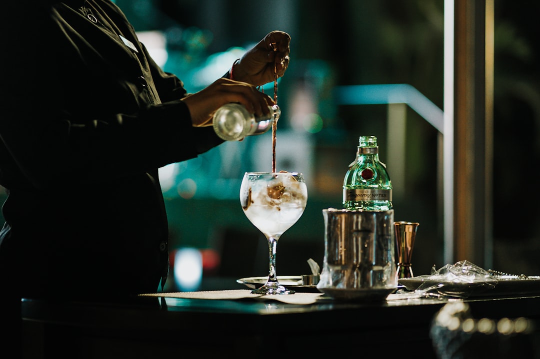 Un barman versant soigneusement un cocktail signature dans un bar sur le toit à Tokyo, les lumières de la ville se reflétant à travers le verre.