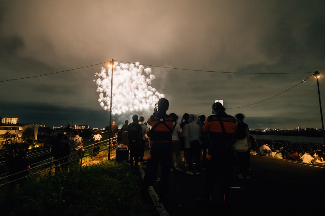 Um grupo de amigos senta-se em um tapete de piquenique e olha para a exibição de fogos de artifício Hanabi Tokyo iluminando o céu noturno de verão.