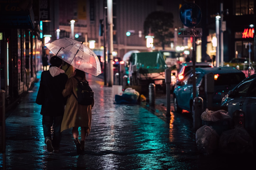 Una donna cammina per una strada di Tokyo tenendo un ombrello elegante durante la stagione delle piogge, vestita con abiti leggeri e traspiranti.