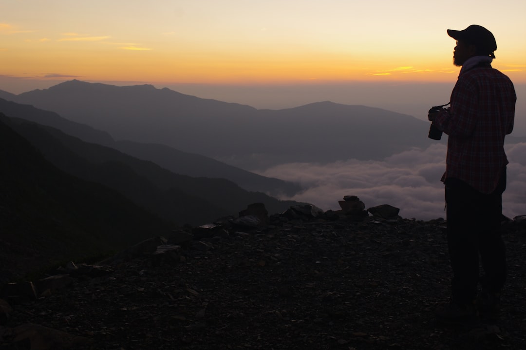 Un grimpeur solitaire observe le lever du soleil goraikō depuis le sentier supérieur pendant la saison d'ascension du mont Fuji, enveloppé dans une veste thermique.