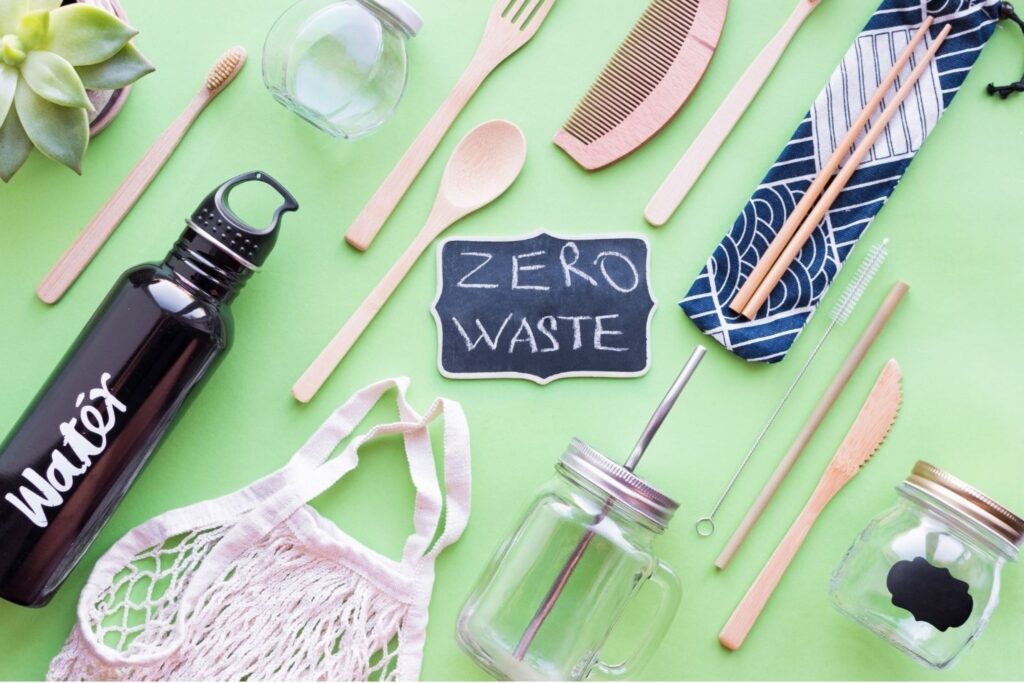 Eco-friendly zero waste starter kit with glass jars, bamboo cutlery, and reusable bottle on green background