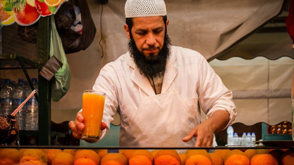 Um vendedor em uma barraca de mercado marroquino entregando um copo de bebidas marroquinas refrescantes a um cliente em um dia quente de verão