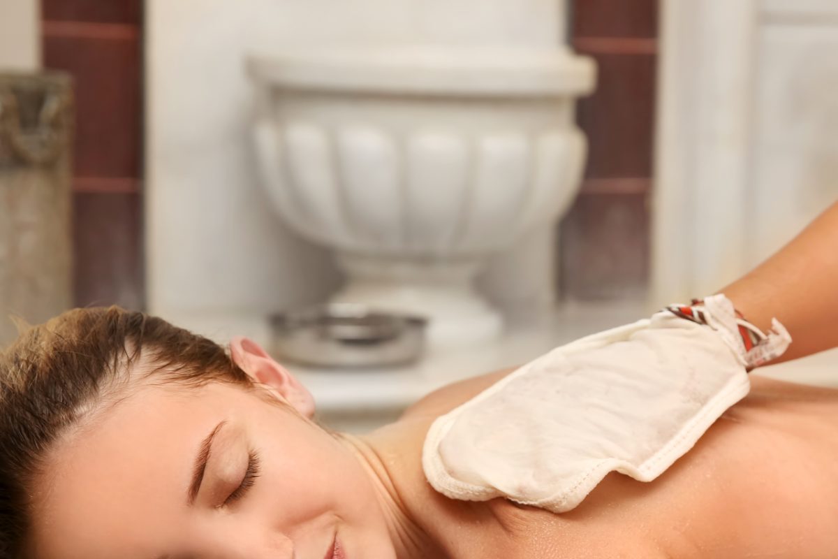Um atendente habilidoso realiza a esfoliação ritual do hammam usando uma luva kessa em um cliente em um espaço de bem-estar marroquino.