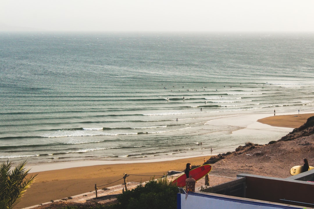 Un surfeur porte une planche dans un village marocain après une session du matin, montrant la vie lors du surf au Maroc en été