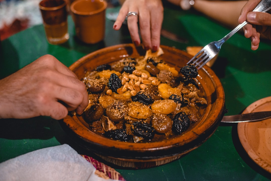 A man tears Moroccan bread to scoop from a steaming Moroccan tagine served in a clay pot at the table.
