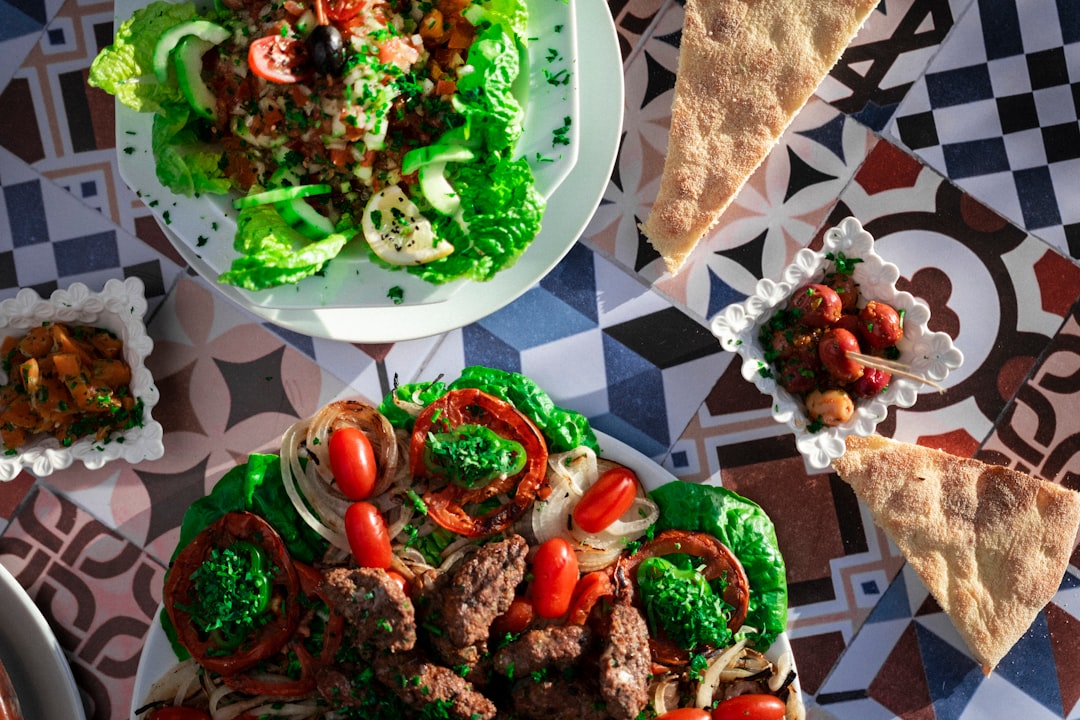 A person placing a bowl of zaalouk on a table spread with colorful Moroccan dishes