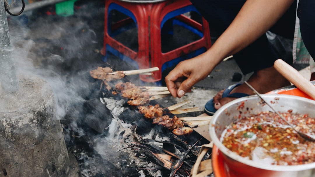 Una famiglia marocchina riunita attorno a una griglia a carbone per una sessione di cucina estiva, preparando spiedini di kefta in un cortile
