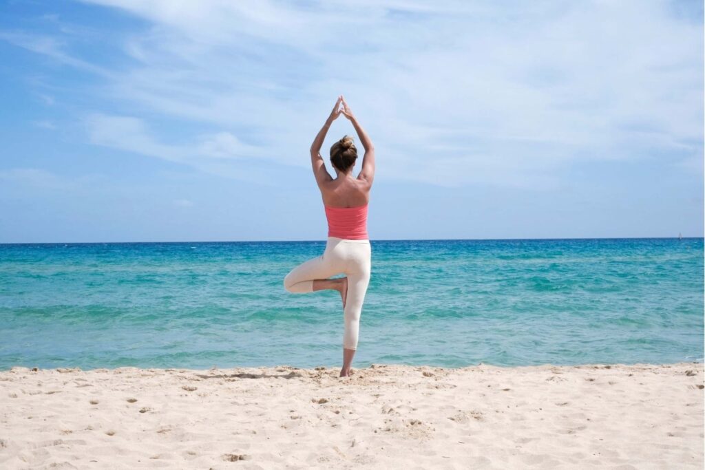 Woman doing yoga on beach mindfulness retreats wellness meditation luxury balance