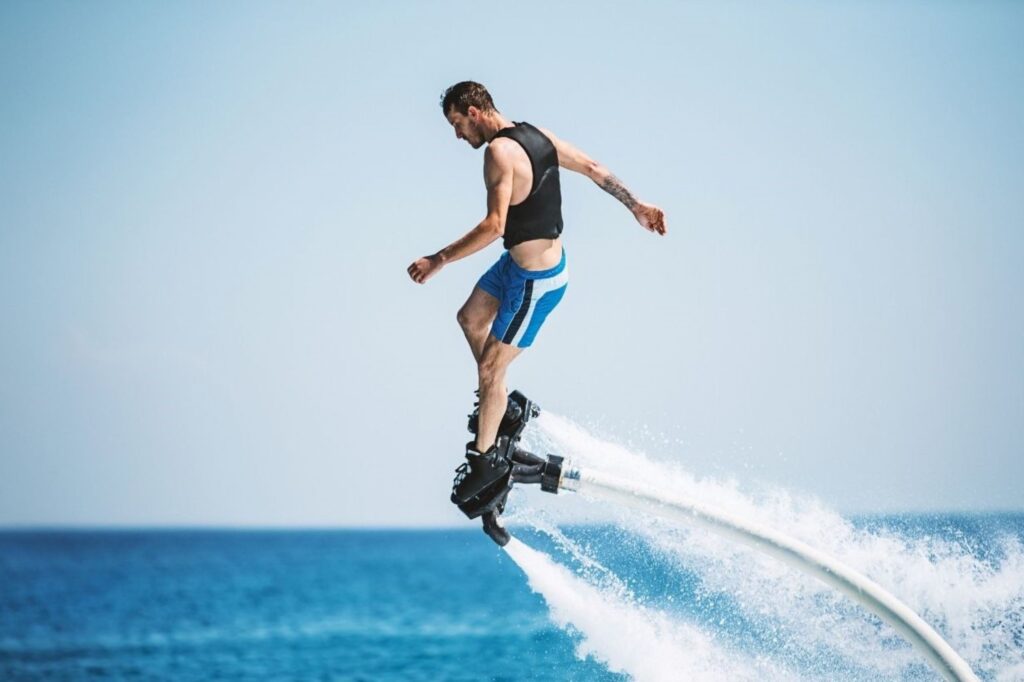Athlete performing flyboarding beach sports near Burj Al Arab Dubai, demonstrating extreme water activities propelling riders above Arabian Gulf through powerful jet pack technology