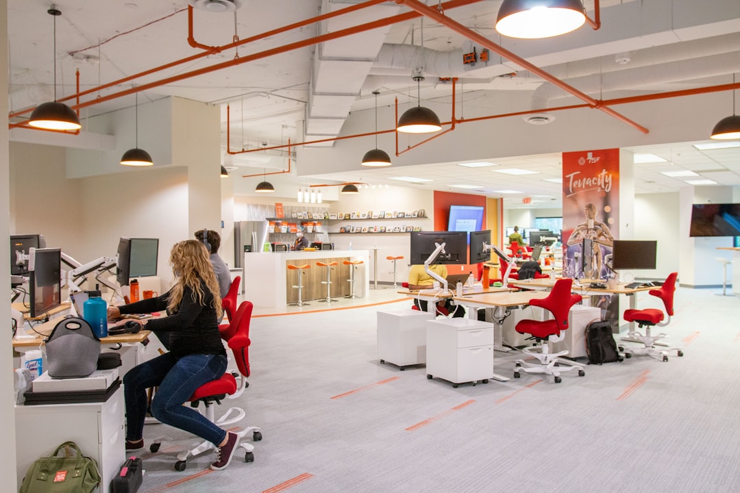 A female startup founder smiling at her laptop in a vibrant co-working space in Dubai, surrounded by other professionals.