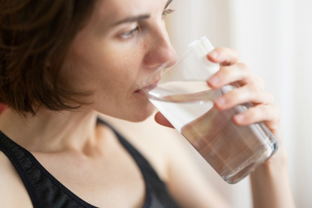 A woman drinking water to maintain hydration as a core part of her daily skincare regimen during Dubai's cooler autumn season