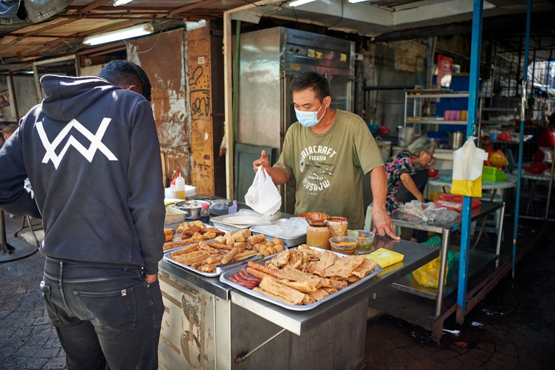 A hawker stall cook ladling rich coconut broth into a bowl of laksa for a customer