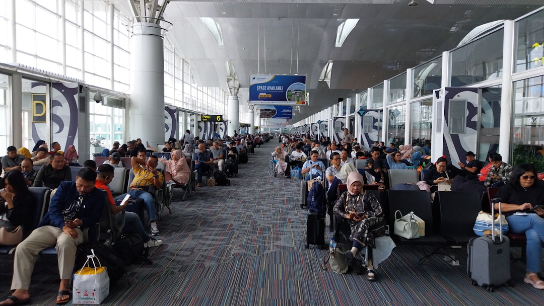 A group of travelers sitting in a departure lounge at one of the London airports, checking phones and travel documents.
