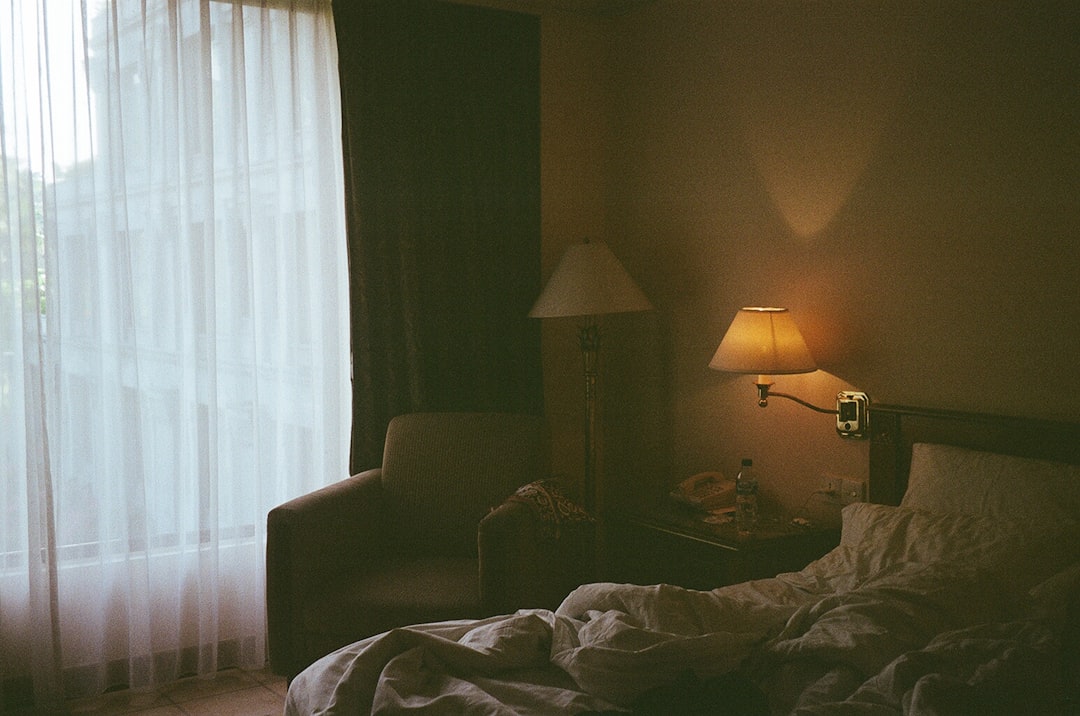 A person dimming a bedside lamp in a dark bedroom as part of a consistent sleep routine before a late-summer London night