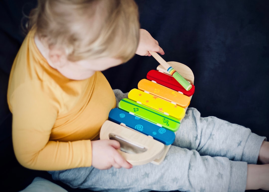 A toddler shaking a tambourine during kids workshops at a music session, sitting alongside a parent and workshop leader.