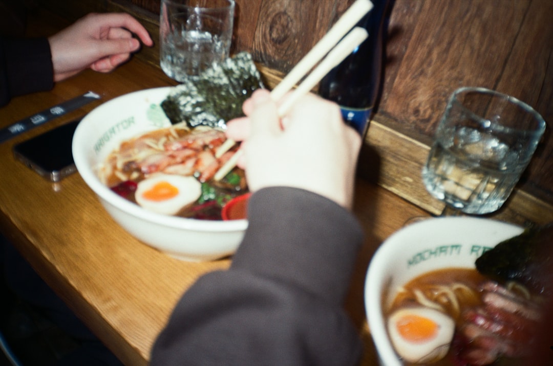2 friends share a table at a London ramen restaurant, smiling over steaming bowls of noodles