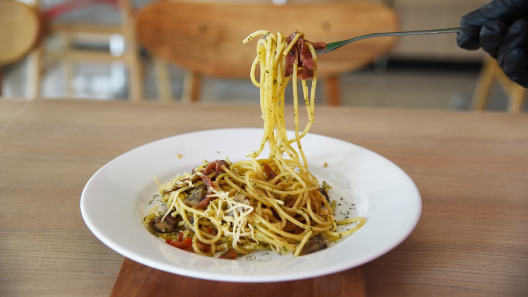 A professional chef plating a refined bowl of gluten-free pasta in a contemporary European restaurant kitchen