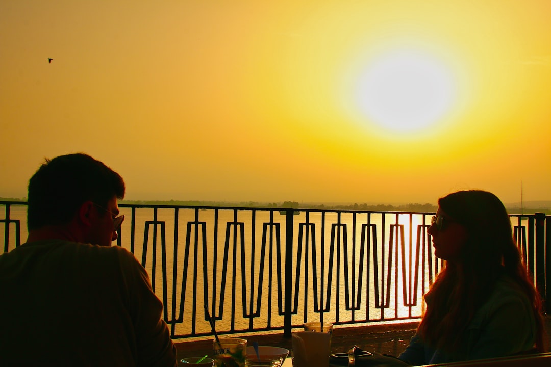 A couple sharing a Mediterranean meal at a rooftop restaurant with a warm EU city skyline visible in the distance