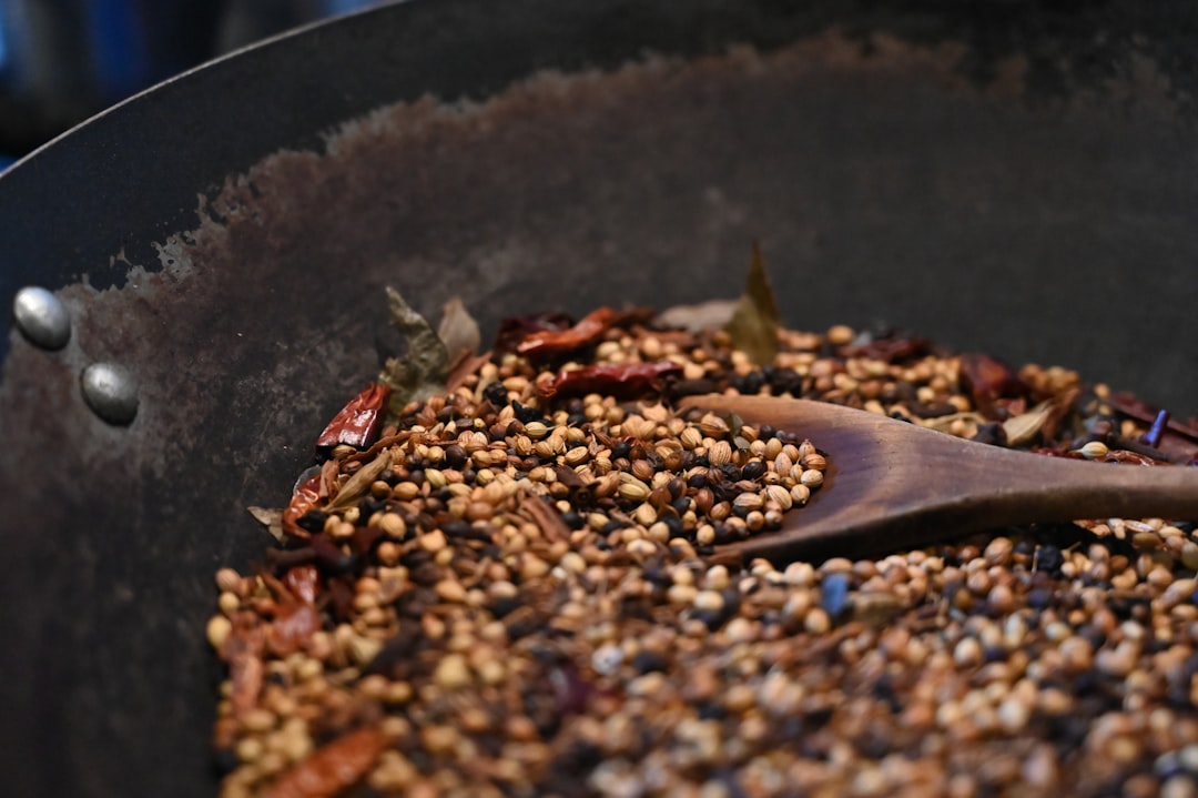 A home cook tempering mustard seeds in a pan as part of a regional spice pantry cooking technique