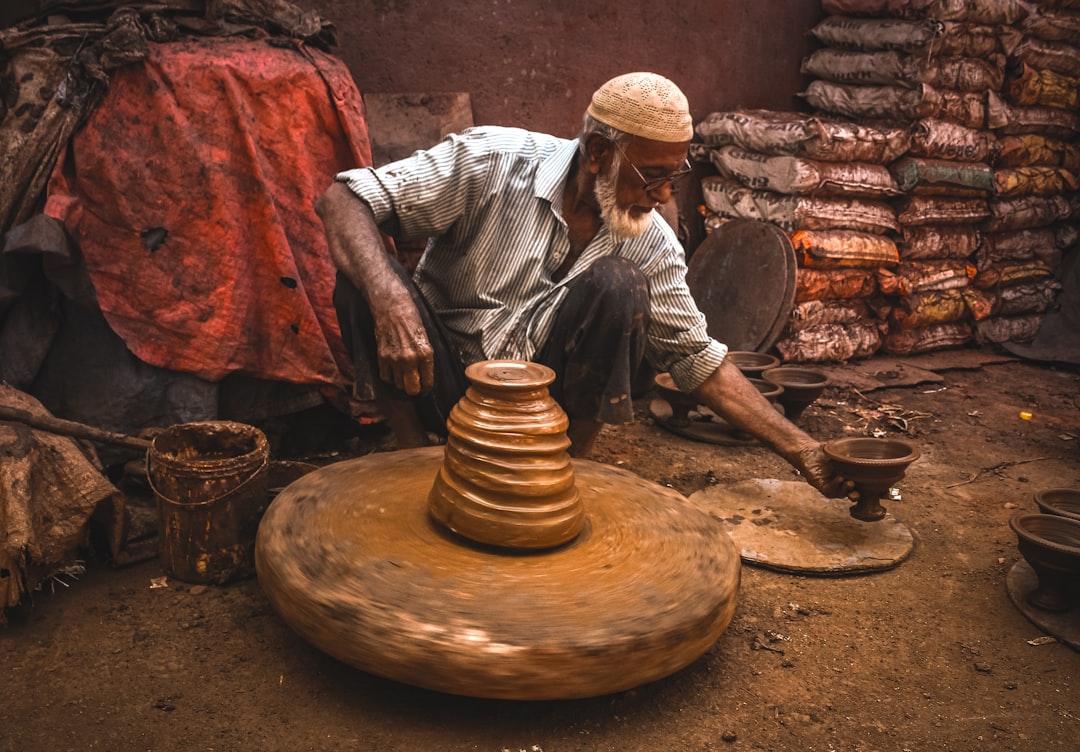 A man grinding whole spices from his spice pantry using a traditional stone grinder in an Indian kitchen